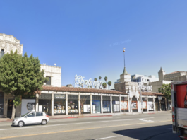 Street view of a historic building with "Chapman Market" signage, large trees, and a clear blue sky.